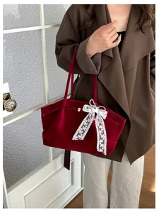 Lifestyle view of a burgundy velvet tote with a white lace bow, carried over the shoulder