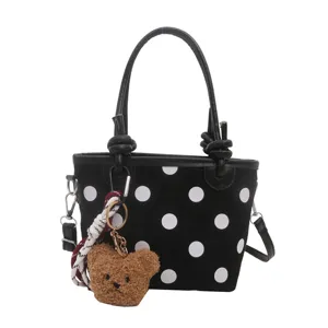 Borsa nera a pois bianchi con manici, tracolla e ciondolo a forma di orsetto, su sfondo bianco