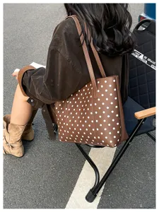 Borsa marrone a pois bianchi con doppi manici lunghi, mostrata su una modella seduta all'aperto
