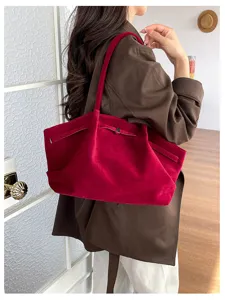 A woman carries a deep red suede tote over her shoulder, showing its soft texture and slim straps