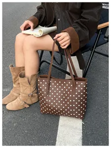 Borsa marrone a pois bianchi tenuta da una modella seduta, con lunghi manici, all'aperto