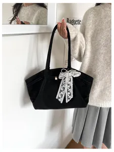 Black velvet bag held by a model, featuring a white lace and pearl bow on the front