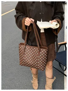Scena di strada con una borsa marrone a pois bianchi portata da una donna con un libro aperto