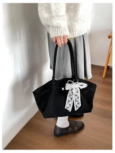 Lifestyle view of a model holding a black tote with a white lace pearl bow and gold-tone clasp