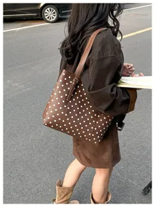Borsa marrone a pois bianchi portata a spalla in una scena di strada urbana quotidiana