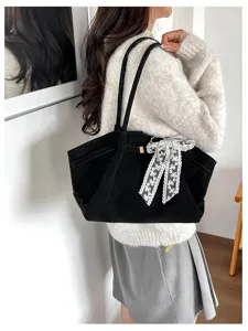 Side view of a model carrying a black tote over her shoulder, with a white lace ribbon bow