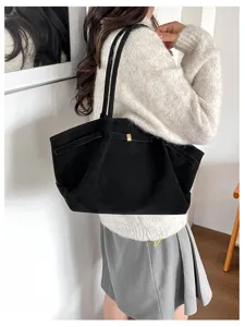 Black tote bag worn over the shoulder, with a slim front accent strap and a small gold-tone clasp.