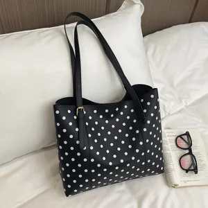 Borsa nera a pois bianchi, chiusura dorata e manici lunghi, sul letto accanto a un libro aperto