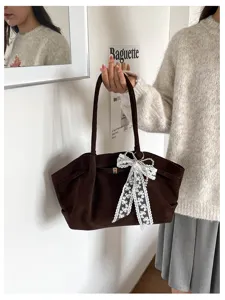 A model holds a soft brown suede-look tote, finished with a white lace bow and pearl accents.