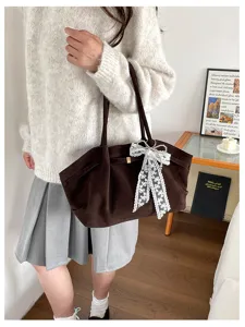 A model carries a brown suede-look tote with long handles and a white lace bow charm indoors