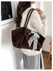 Side view of a woman carrying a brown suede tote with long handles and a white lace bow