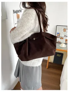 Dark brown suede tote worn over the shoulder, with a wide body and a small metal clasp.