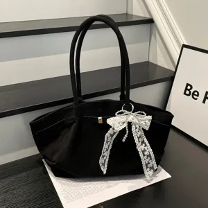 Black fabric bag with long handles, white lace and pearl bow, and a metal clasp on a dark table