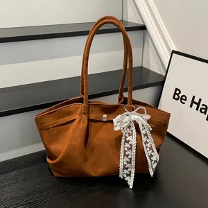 Brown suede-textured bag with twin handles, metal clasp and a white lace bow charm on display