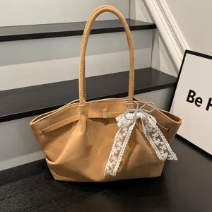 Detail view of a tan suede-look bag with gold clasp, white lace bow and pearl charm