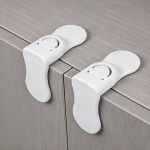 Pair of white plastic child safety cabinet locks shown fitted along the edge of a gray cabinet