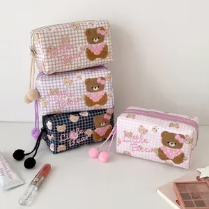 Karierte Kosmetiktaschen mit Teddybärstickerei und Bommelanhängern liegen auf einem weißen Tisch