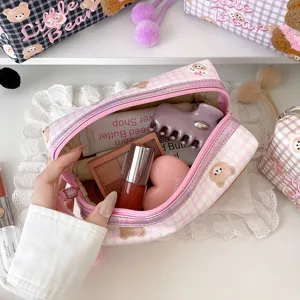 Offene rosa Tasche mit Karomuster und Kosmetikartikeln, in die eine Hand hineingreift