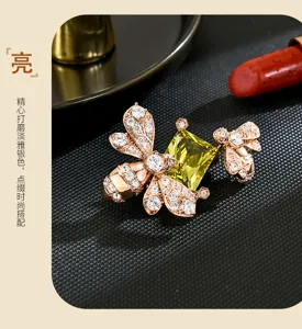 Dettaglio di spille ape color oro rosa, con cristalli e gemma quadrata giallo-verde su tessuto scuro