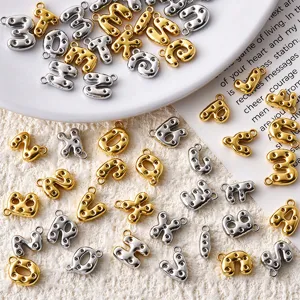 Close-up of gold and silver bubble-letter charms with loop details, scattered on a plate and cloth