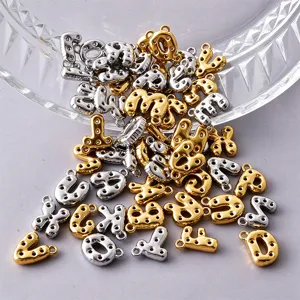Gold and silver bubble-letter charms with round cutouts and small loops, piled on a clear dish