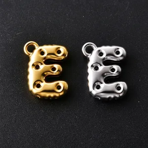 Close-up of gold and silver bubble-style letter E charms with raised shapes and round hanging loops