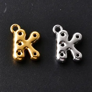 Close-up of two bubble-style K-shaped charms in gold and silver, each with four holes and a loop
