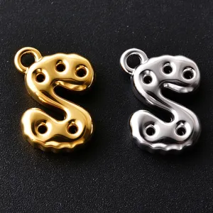 Close-up of gold and silver S-shaped letter charms with loop rings and circular cutouts on black