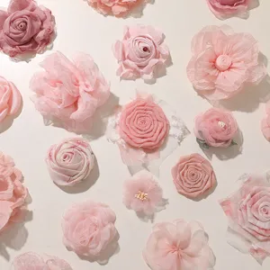 Assorted pink sheer fabric flowers, including roses and layered blooms, arranged on a white surface