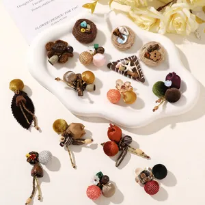 Assorted handmade earrings with woven fabric balls, wooden accents and beads arranged on a white tray