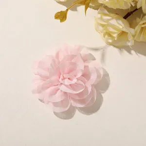 Overhead view of a layered pink chiffon flower with softly ruffled petals on a cream surface