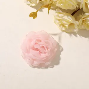 Close-up of a layered pale pink fabric rose with soft sheer petals on a light neutral surface