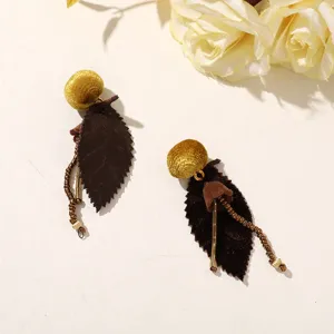 Pair of dark brown leaf earrings with gold ball tops and bead accents on a pale surface