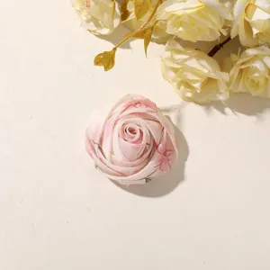 Close-up of a layered pink floral fabric rose on a cream surface with ivory flowers nearby