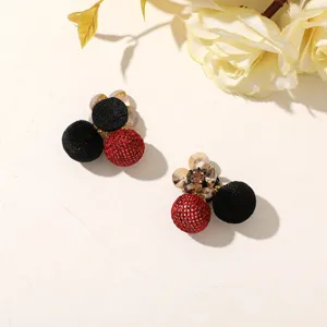 Close-up of black velvet and red woven ball earrings with crystal flower studs on a pale surface.