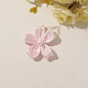 Flat lay of a pink satin five-petal flower with a pearl-like center on a beige surface