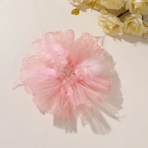 Flat lay of a pink feather and tulle flower with a beaded, sequin-accented center on white