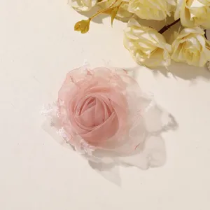 Close-up of a layered pink tulle rose with white mesh accents, arranged on a pale surface.