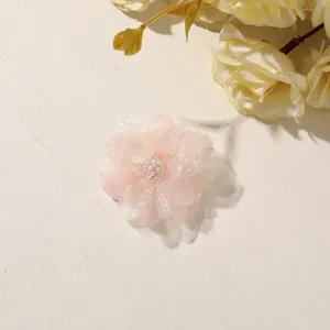 Overhead view of a pink tulle and lace flower with tiny white pearl accents, on a cream background