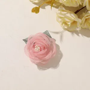 Close-up of a pink layered tulle flower with pearl-like center beads and gray-green leaves