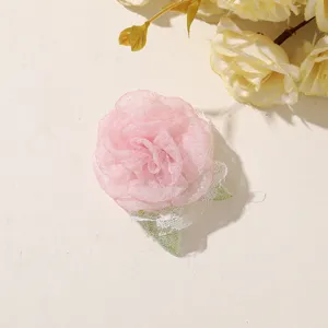 Pink sheer fabric flower with white lace edging and green leaves, photographed on a light background