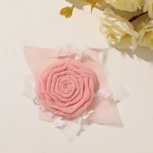 Close-up of a pink fabric rose with white tulle and soft trim, arranged flat on a light surface