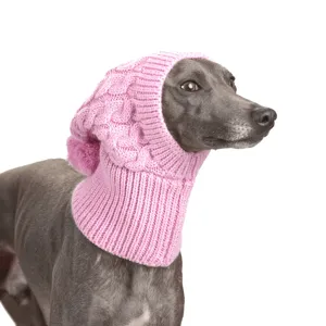 Grijze hond van opzij met een roze kabelgebreide muts en pluizige pompon tegen witte achtergrond