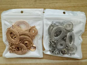 Twee doorzichtige zakjes tonen gouden en zilveren opengewerkte ronde hangers met kettingen op hout
