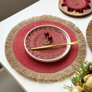 Round red woven placemat with jute fringe and gold accents, styled with a white plate and cutlery
