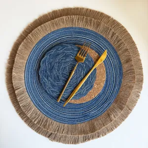 Round blue-and-white woven placemat with natural jute fringe, shown overhead with gold cutlery