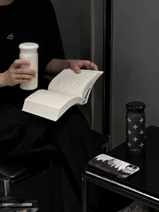 Una persona legge con un bicchiere bianco decorato; un modello nero a fantasia è sul tavolo.