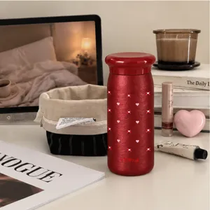 Tazza rossa metallizzata con coperchio arrotondato e piccoli cuori rosa, su una scrivania
