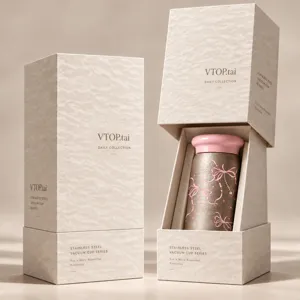 Scatola regalo accanto alla confezione aperta, con tazza dal coperchio rosa e motivo a fiocco
