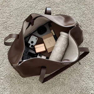 Mini tazza termica in titanio dentro una borsa tote marrone aperta, con oggetti quotidiani